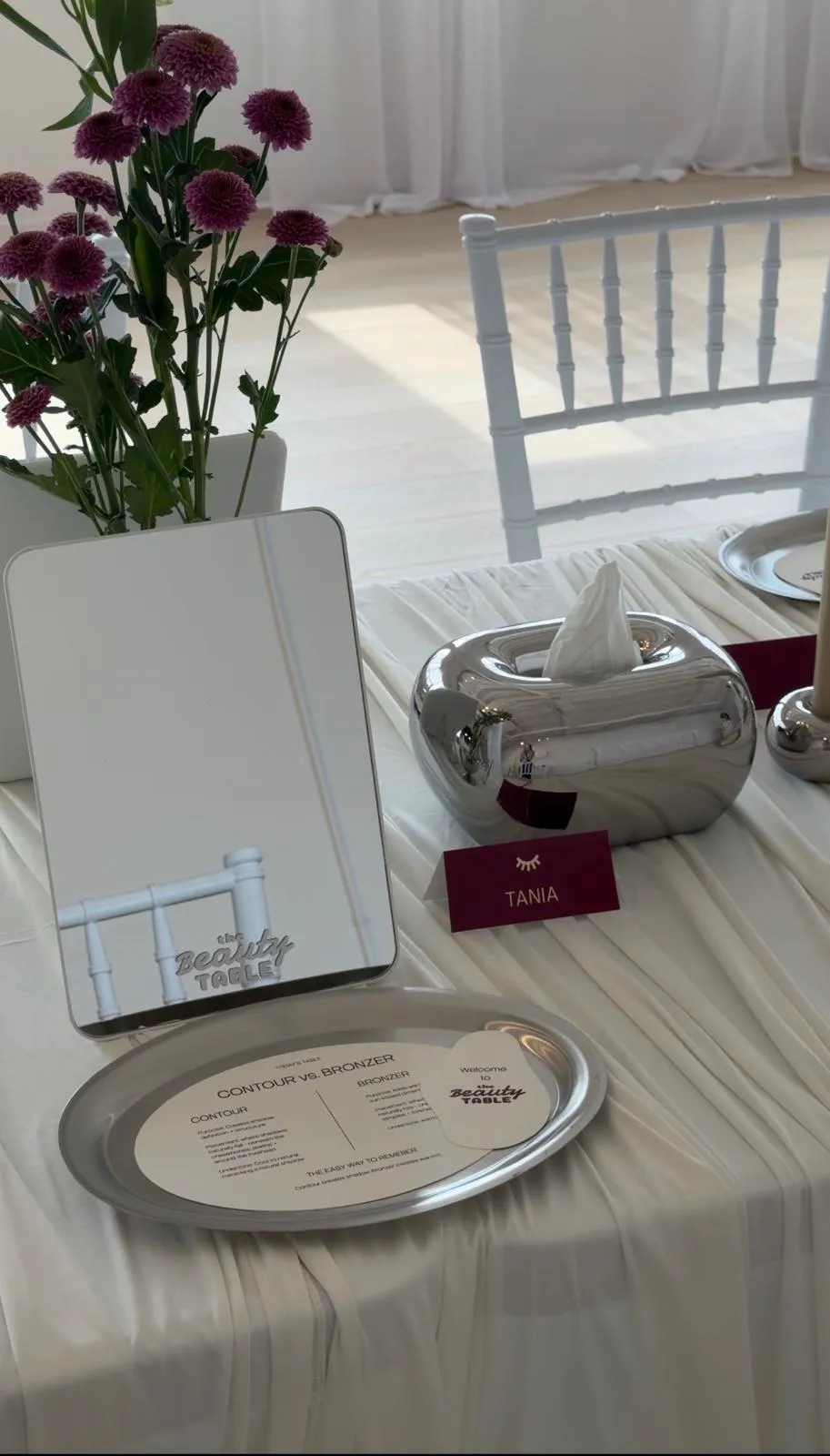 A place setting waiting for a guest: a tabletop mirror, a personalized name card, a welcome card and a printed contour vs. bronzer guide on a silver tray.