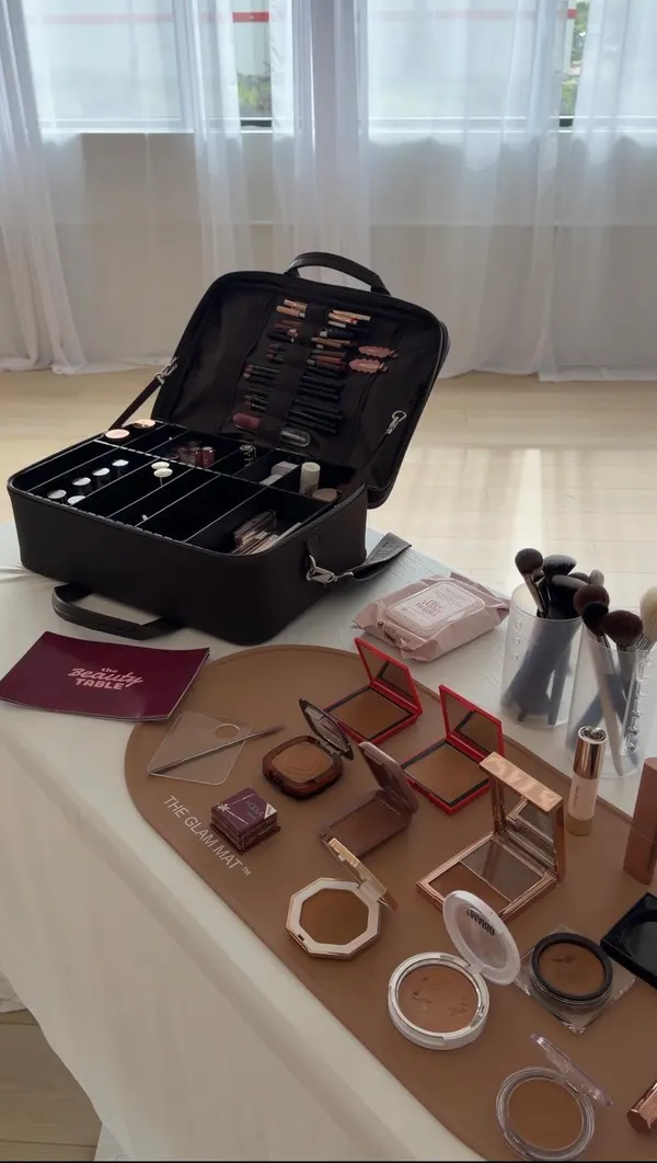 An open makeup artist's kit beside a spread of bronzer and contour compacts laid out on a glam mat, with brushes ready to use.